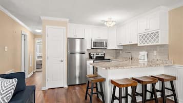 A kitchen with white cabinets, a stainless steel refrigerator, a microwave, a stove, and a coffee maker. There are wooden stools at the island.