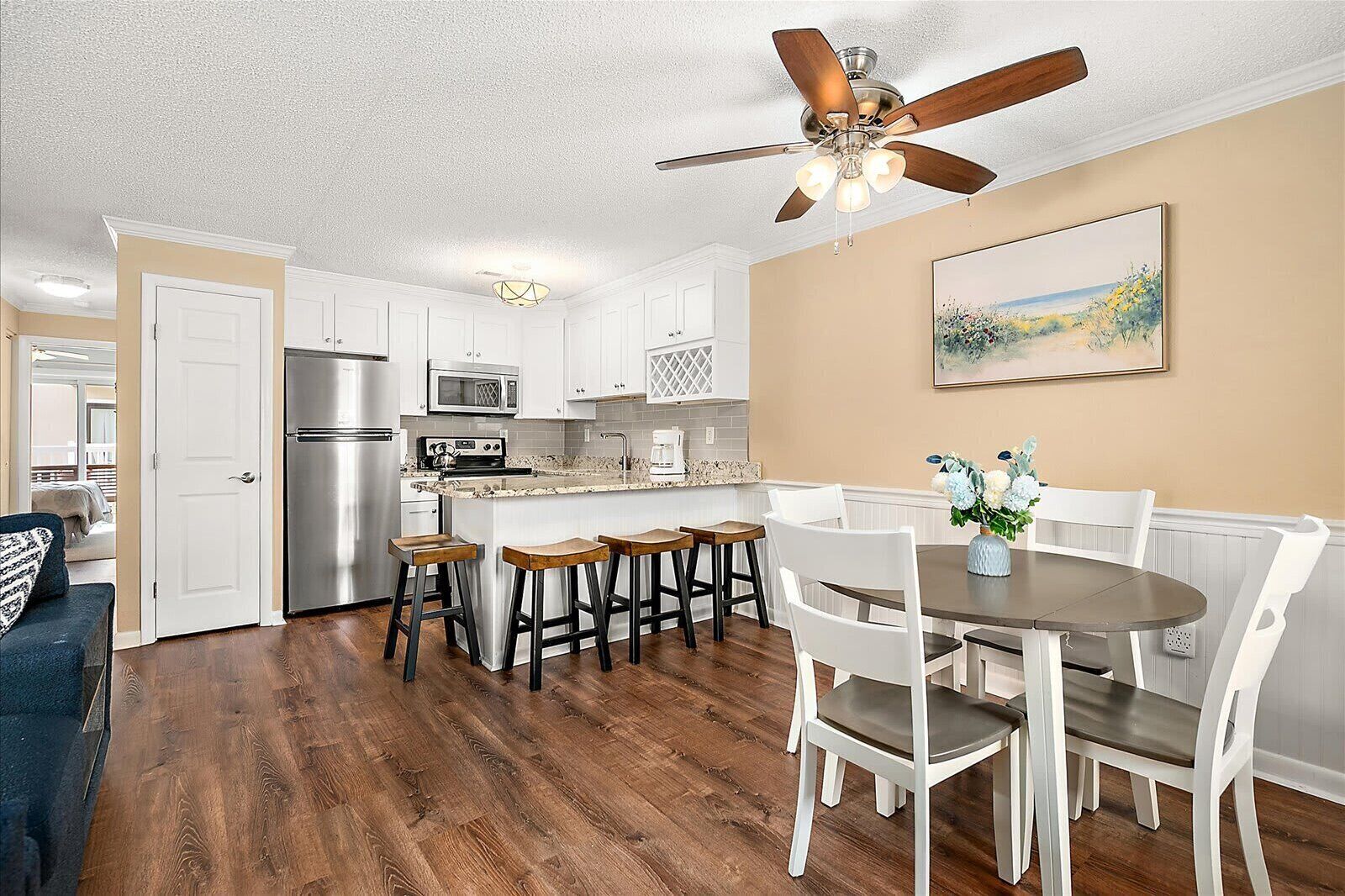 A modern kitchen with white cabinets, a stainless steel refrigerator, a microwave, and a ceiling fan.