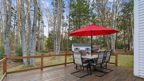 A wooden deck with a table and chairs, a red umbrella, and a house in the background. - 1.5 Miles to Kennebunk BEACH|Sleeps 12| Pet friendly (Kennebunk)