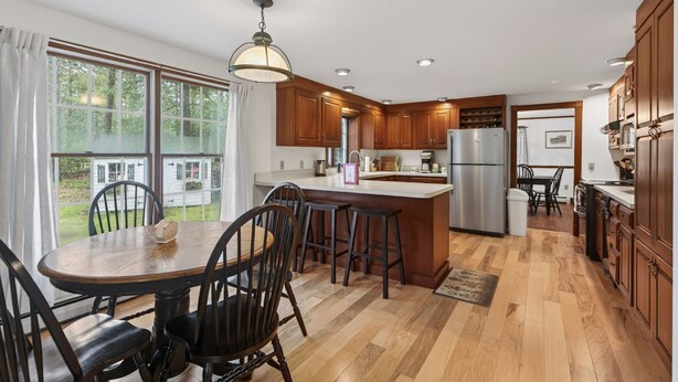 A kitchen with wooden cabinets, a central island, bar stools, and a dining table with chairs. - 1.5 Miles to Kennebunk BEACH|Sleeps 12| Pet friendly (Kennebunk)