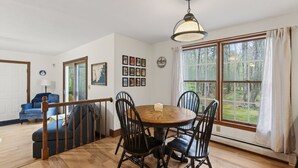 A dining area with a round table, black chairs, a wooden floor, a hanging light fixture, and a window with curtains. - 1.5 Miles to Kennebunk BEACH|Sleeps 12| Pet friendly (Kennebunk)