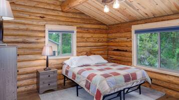Une chambre à coucher située dans une cabane en rondins, avec un lit, deux fenêtres, une lampe et une commode.