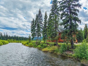 Una cabaña junto a un río, rodeada de altos árboles.