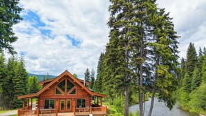 A log cabin with a deck, surrounded by a lake and forest.