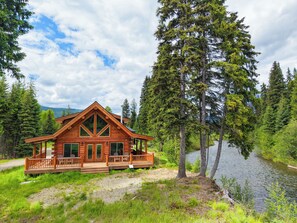 A log cabin with a deck, surrounded by a lake and forest.
