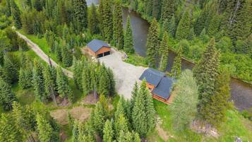 Une cabane avec une allée en gravier, entourée d’une forêt dense et bordée par une rivière.