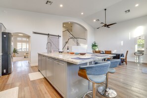 A spacious kitchen with a central island, bar stools, and a dining area with a table and chairs. - Upscale Chandler Executive Home | Resort Backyard (Chandler)