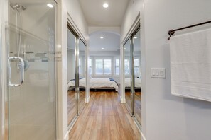 A modern hotel room with a glass shower enclosure, a wooden floor, a bed with white bedding, and a large window providing natural light. - Upscale Chandler Executive Home | Resort Backyard (Chandler)