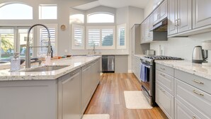 Une cuisine moderne dotée d’un grand îlot central, d’appareils électroménagers en acier inoxydable et offrant une vue sur l’extérieur.
