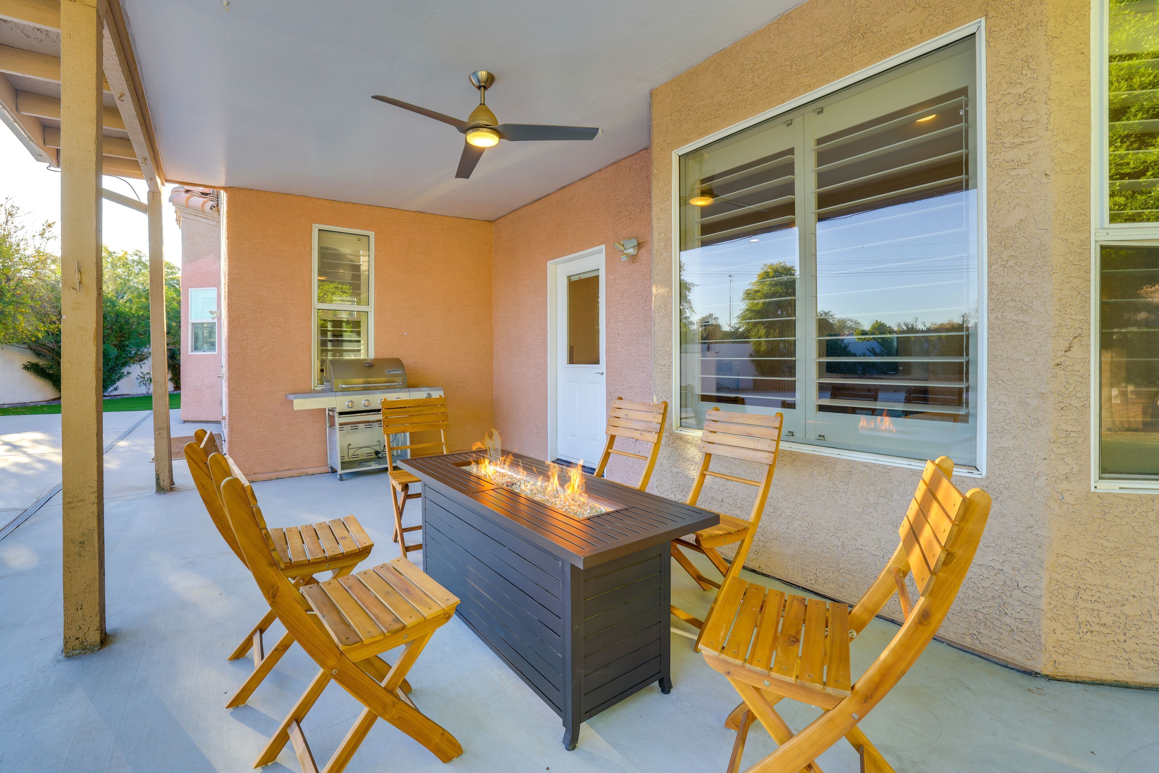 Une terrasse extérieure avec une table rectangulaire, des chaises en bois, un ventilateur de plafond et une vue sur la rue.