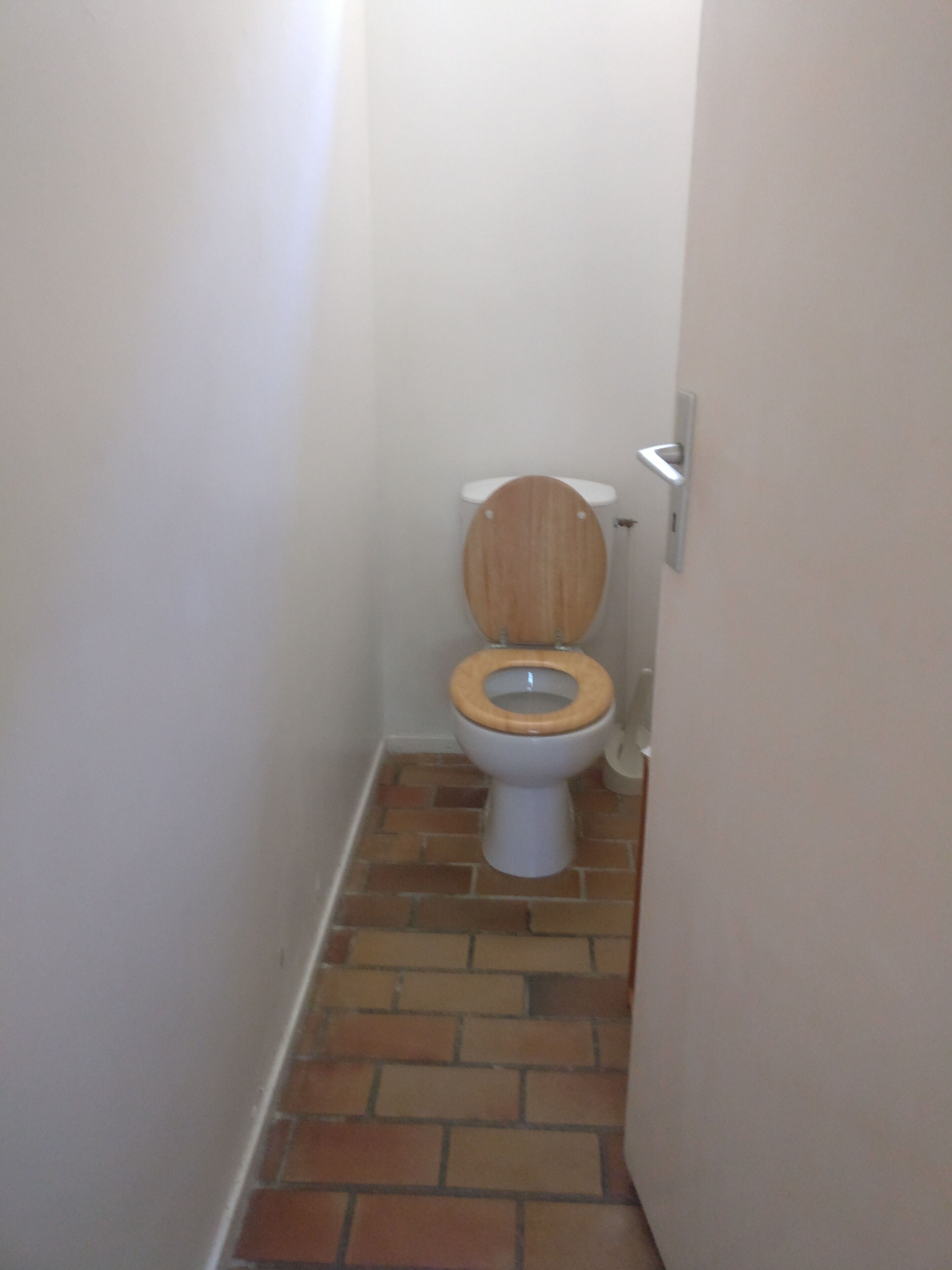 A small bathroom with a toilet, a wooden seat, and a tiled floor.