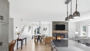 A modern kitchen with a stone fireplace, dining area, and a large island. - Rustic-Modern Gem | Steps to Blue Mtn Village (The Blue Mountains)