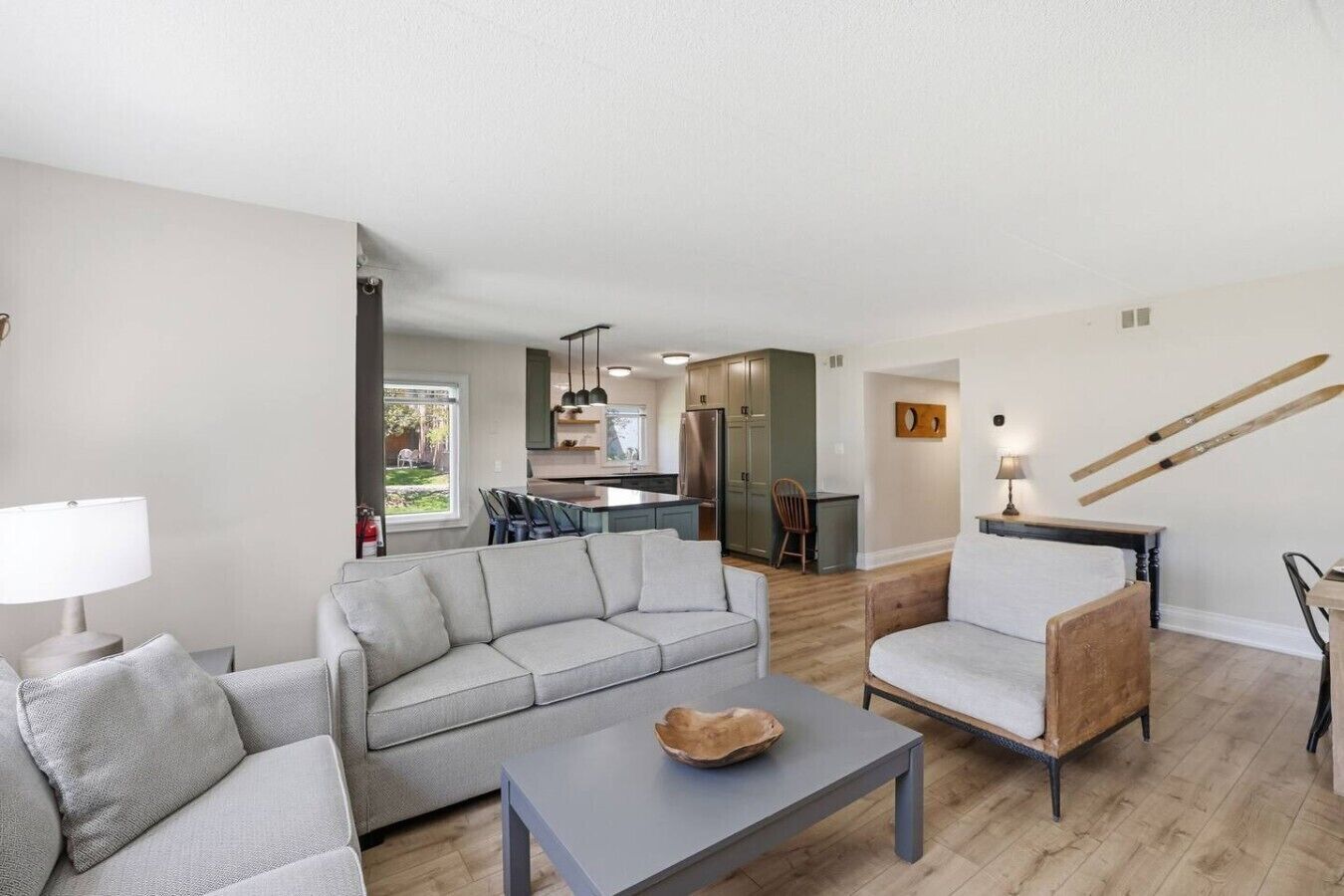 A modern living room with a gray sofa, a wooden chair, a coffee table, and a kitchen in the background.