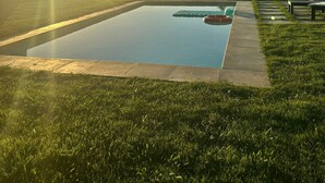 Ein rechteckiger Pool mit Blick auf sanfte Hügel inmitten von Gras und einer Betonplattform.