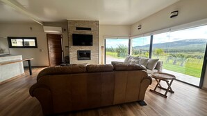 Ein modernes Wohnzimmer mit einem großzügigen Ecksofa, einem Kamin, einem Flachbildfernseher und einem großen Fenster mit Blick auf die Landschaft.
