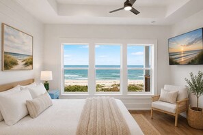 Ein Schlafzimmer mit einem großen Bett, einem Sessel, einer Lampe und Blick auf den Strand.