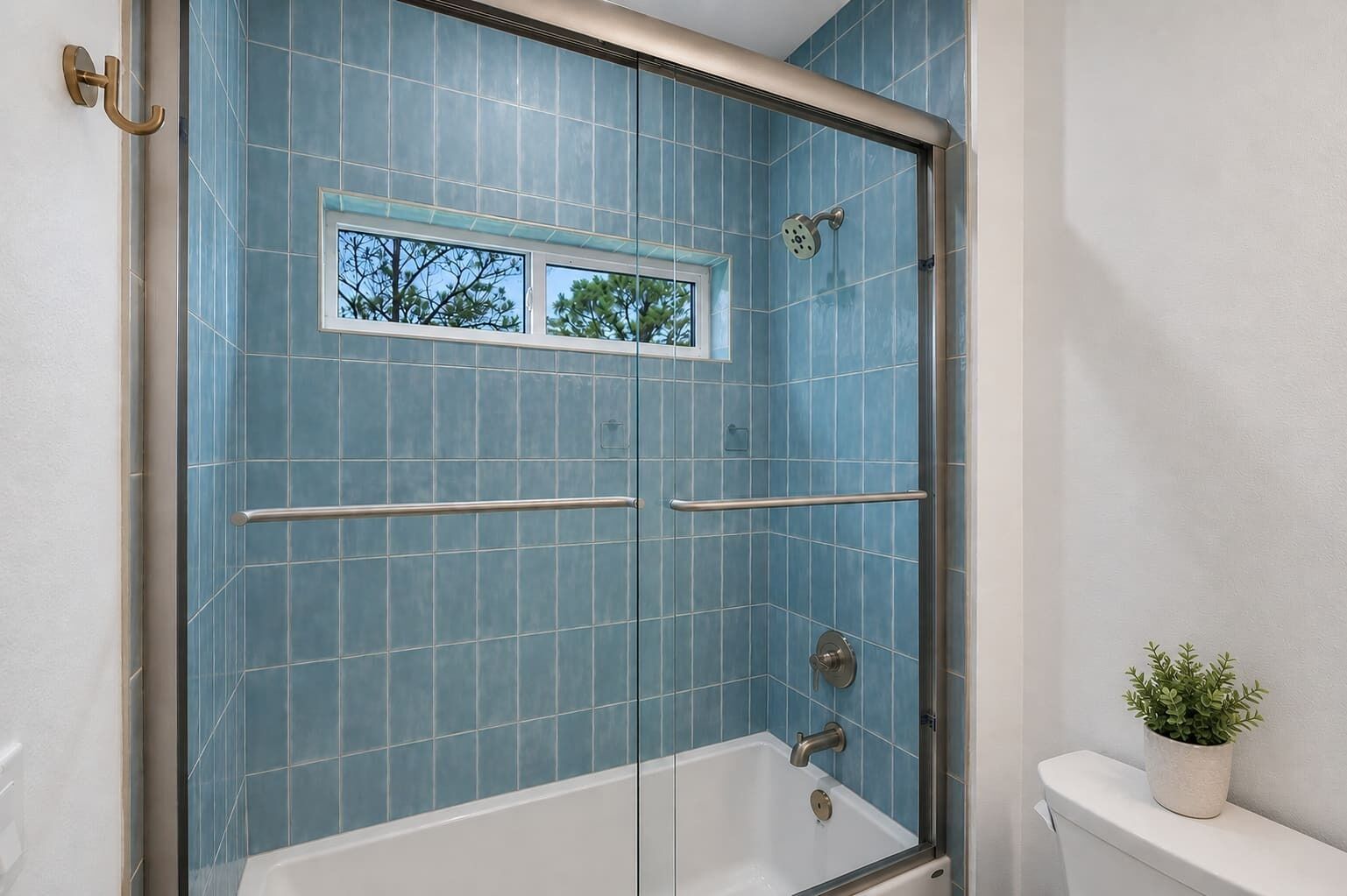 Un baño con cabina de ducha, una ventana y una planta en maceta.