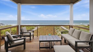 A covered outdoor deck with a view of the ocean, featuring a wooden table, two sofas, and two chairs. - NEW- 6 bedroom-Private Pool- Pet Friendly (Saint George Island)