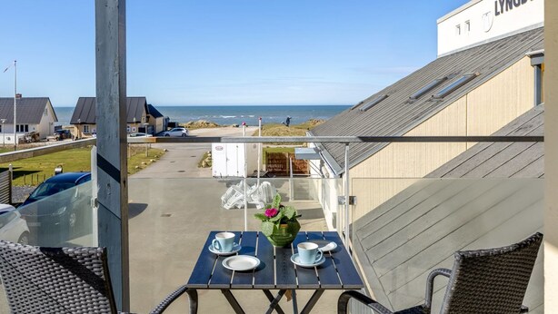 Ein Balkon mit Tisch für zwei Personen, der Blick auf einen Strand und ein Gebäude mit der Aufschrift 'LYNGBY' gewährt.