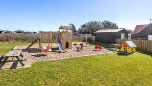 Ein Spielplatz mit Rutsche, Schaukeln und einer kleinen Hauskonstruktion.