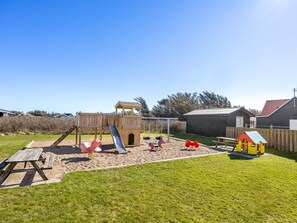 Ein Spielplatz mit Rutsche, Schaukeln und einer kleinen Hauskonstruktion.