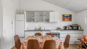 Eine kompakte Küche mit weißen Schränken, einem Herd und einer Mikrowelle. Ein Esstisch mit Stühlen und einer Pflanze steht auf dem Tisch.