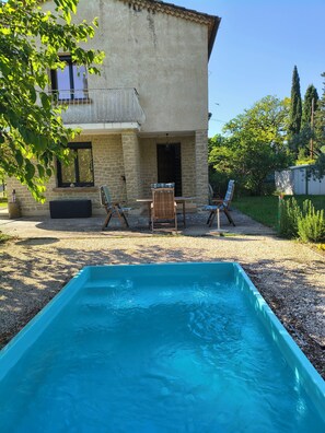 Ein Poolbereich mit einem Steinhaus, Sitzgelegenheiten im Freien und blauem Himmel.
