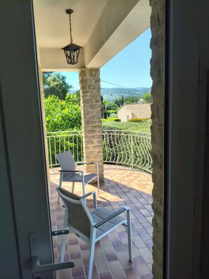 A balcony with two chairs, a hanging light fixture, and a view of greenery and buildings.