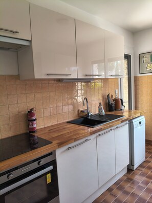 A kitchen with white cabinets, a black countertop, a stainless steel sink, a dishwasher, and a fire extinguisher.