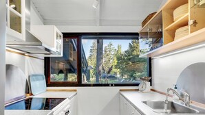 Una cucina compatta con vista dalla finestra, mobili bianchi, un lavandino e un piano cottura.