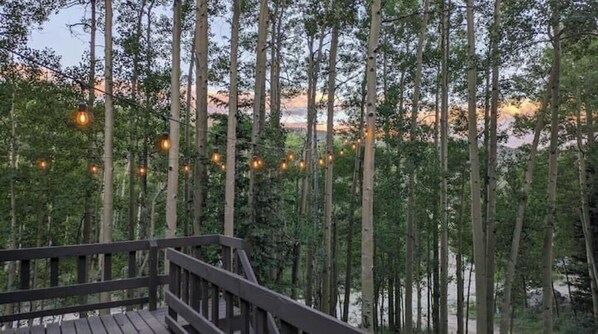 Eine Holzterrasse mit Blick auf hohe Bäume und Lichterketten.