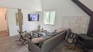 Een woonkamer met een bank, een televisie, een open haard en een raam.