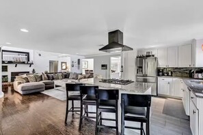 A modern kitchen with a central island, stainless steel appliances, and a dining area with bar stools. - Cape Cod Getaway (Barnstable)