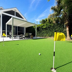 Un terrain de golf avec un pavillon blanc, un drapeau jaune et une balle de golf sur une pelouse artificielle.