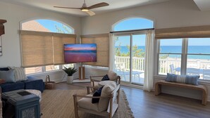 Ein geräumiges Wohnzimmer mit großem Fernseher, bequemen Sitzgelegenheiten und Meerblick.