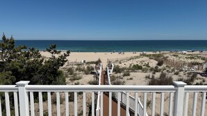 Blick auf einen Strand vom Balkon mit Holzterrasse, Sandstrand und Meer.