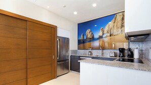 Una cucina moderna con frigorifero integrato, lavastoviglie, piano di lavoro in granito e un grande quadro raffigurante un paesaggio costiero.