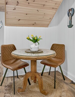 A round table with a white vase and yellow tulips, flanked by two brown leather chairs, set on a woven rug.