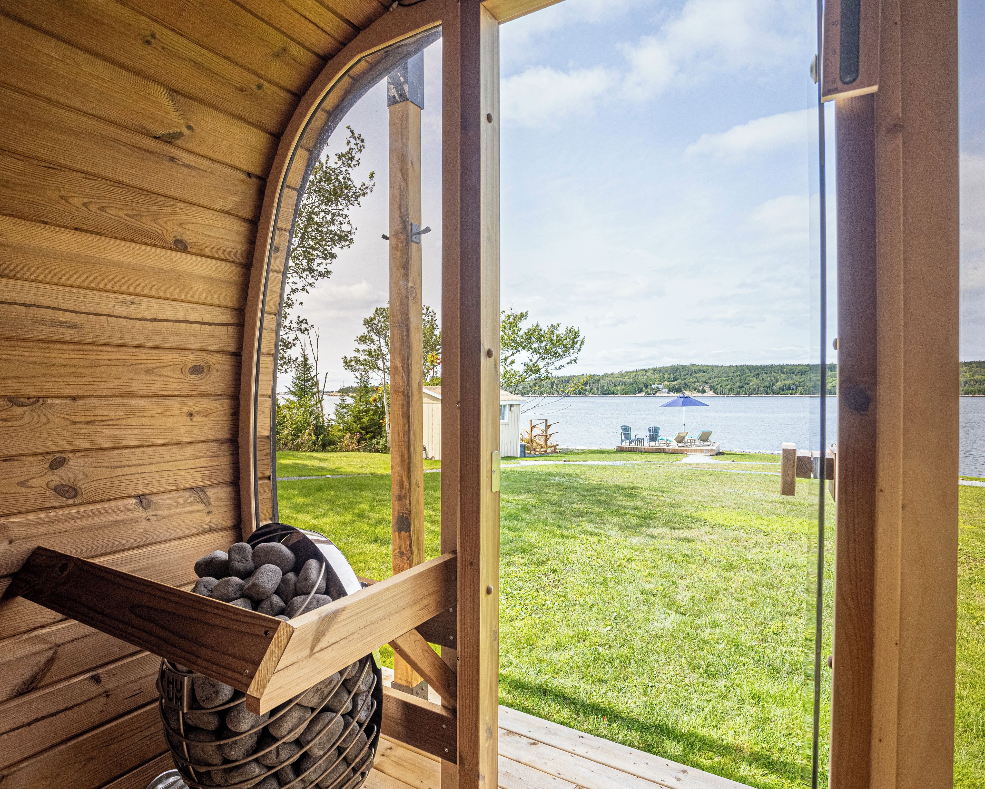 A wooden cabin with a large arched window, a stone fireplace, and a view of a lake with outdoor furniture.