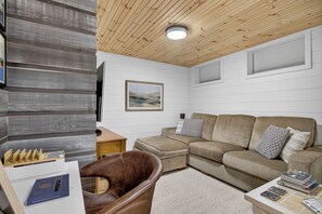 A cozy living room with a sectional sofa, a brown leather armchair, and a flat-screen TV mounted on the wall.