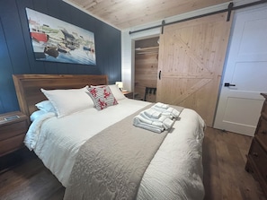 Un dormitorio con una cama, un cuadro, una puerta de madera y una mesita de noche.