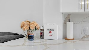 Un meuble blanc avec des poignées dorées, une trousse de premiers secours blanche, un vase avec des fleurs, une boîte de conserve et une bougie posés sur un comptoir en marbre.