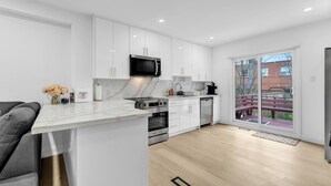Une cuisine moderne avec des meubles blancs, un four à micro-ondes, un four et un lave-vaisselle encastrés, un plan de travail en marbre et une grande porte-fenêtre coulissante donnant sur une terrasse.