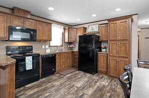 A kitchen with wooden cabinets, a black microwave, a refrigerator, and a stove.