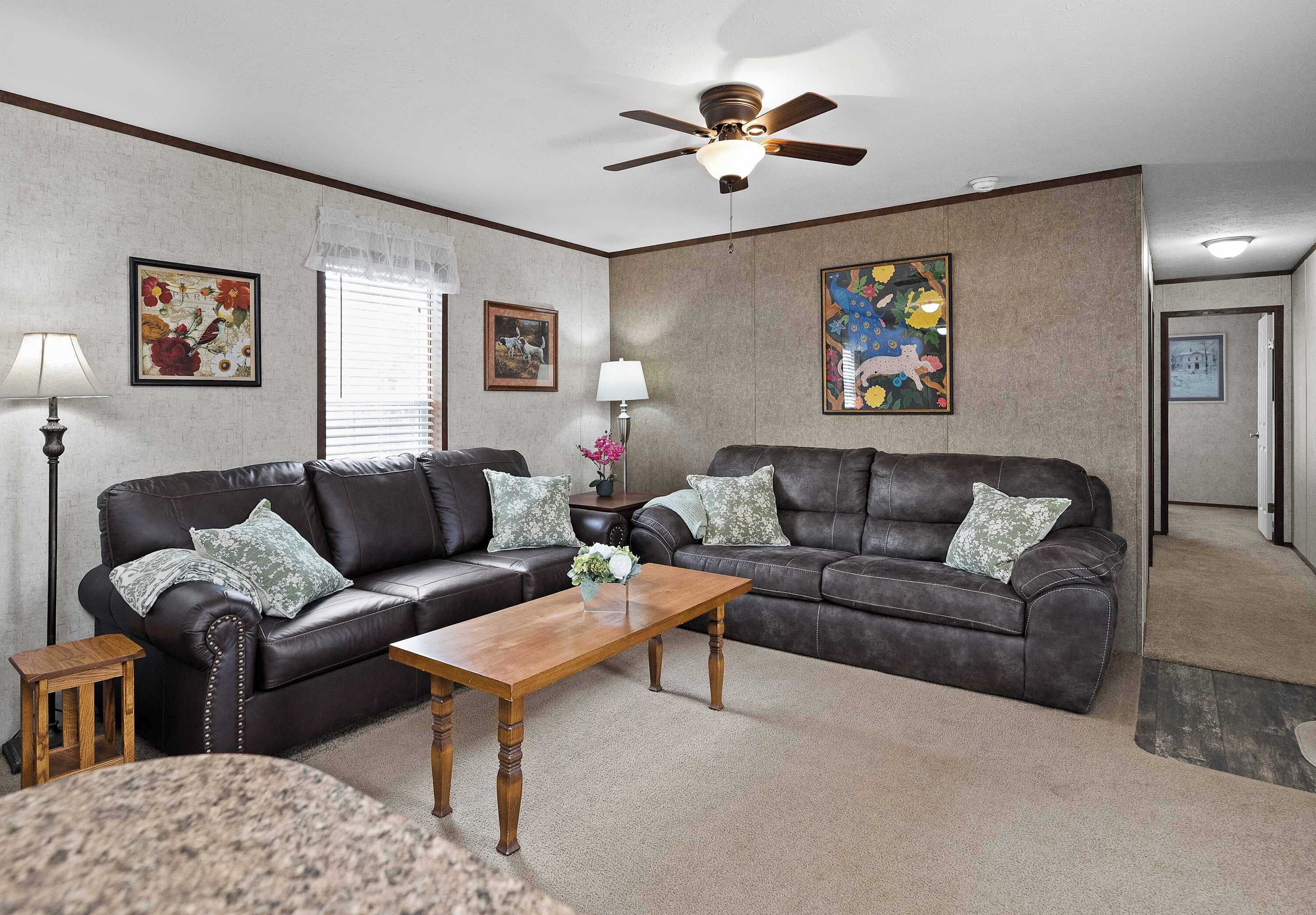 A living room with a dark leather sofa, a wooden coffee table, and a ceiling fan.