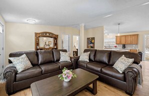 A living room with a brown leather sectional sofa, a coffee table with a floral arrangement, and a wooden cabinet with a mirror.