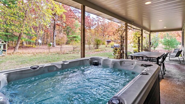 Een hottub in een overdekte buitenruimte met uitzicht op herfstbomen.