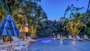 Un espace piscine doté de chaises longues, d’un jacuzzi et de palmiers.