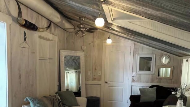 Un dormitorio estilo loft con techos altos, vigas a la vista, una cama grande, dos sofás, una mesita y un espejo.
