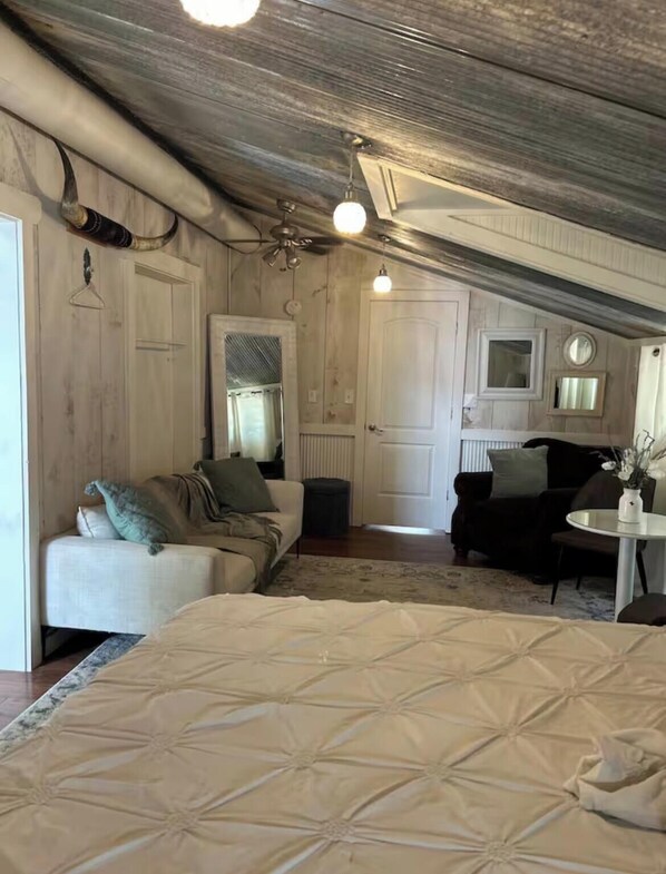 Une chambre de style « loft », avec un plafond haut, des poutres apparentes, un grand lit, deux canapés, une petite table et un miroir.